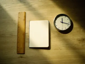 Eiken bureau met open notitieboek, houten liniaal en analoog horloge in zacht ochtendlicht, bovenaanzicht.